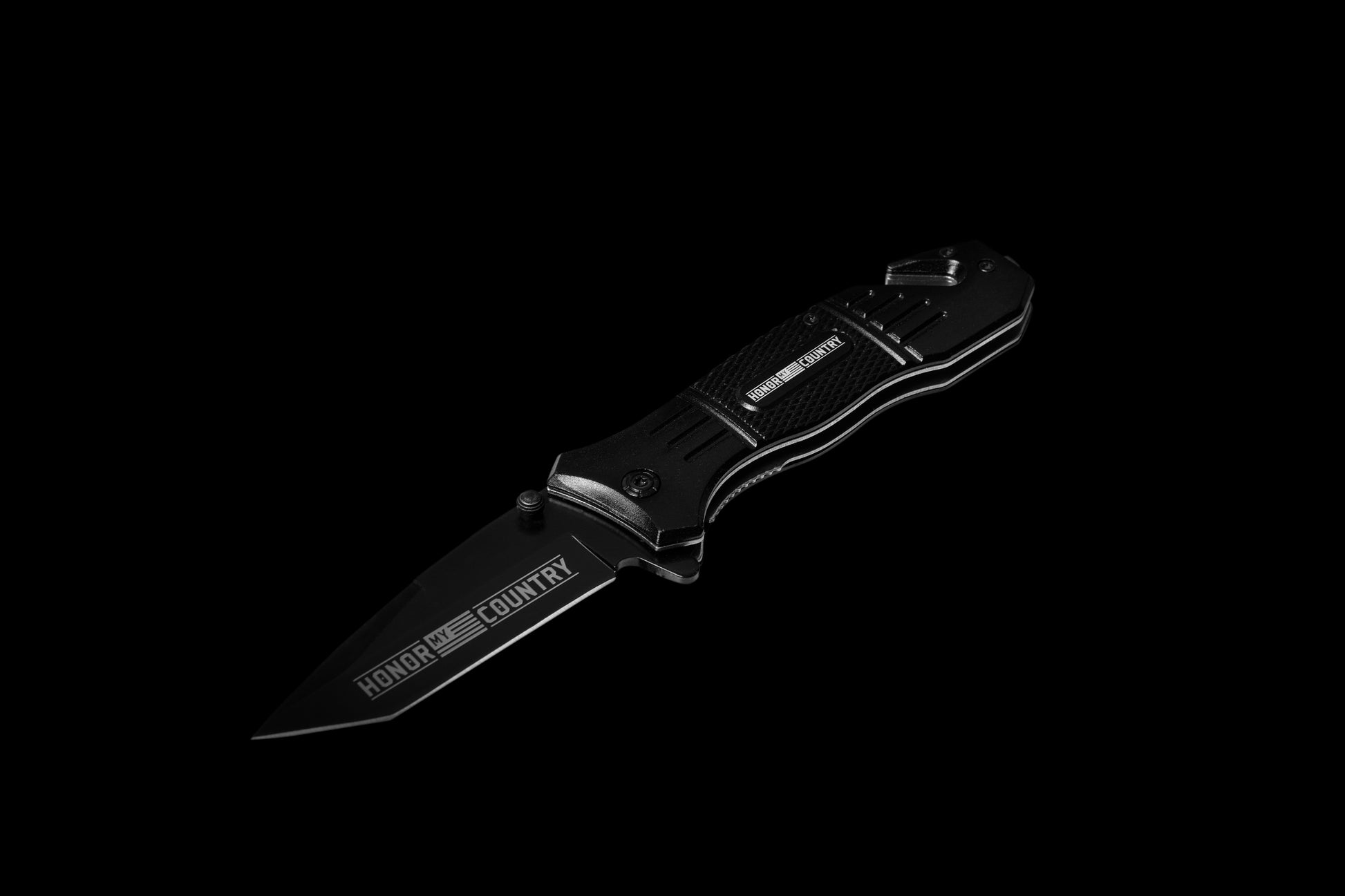 A black folding pocket knife with a partially serrated blade, featuring the 'HONOR' and 'COUNTRY' logo, shown against a solid black background.