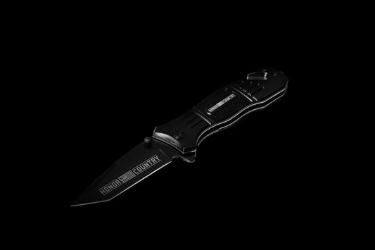A black folding pocket knife with a partially serrated blade, featuring the 'HONOR' and 'COUNTRY' logo, shown against a solid black background.